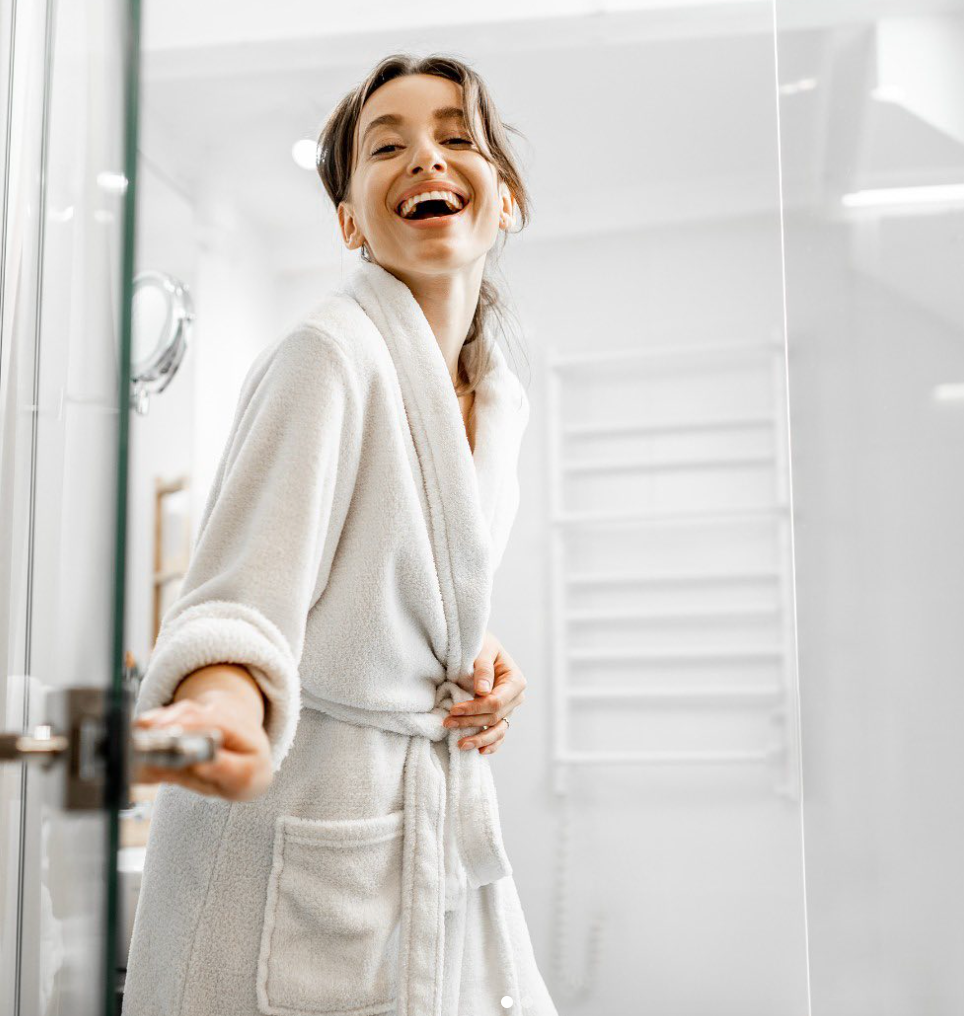 A smiling girl in bathroom doorway dressed in a comfy robe 